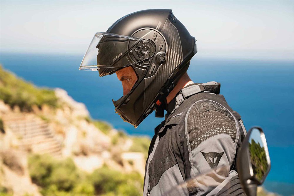 A sport-touring rider donning the Cardo Beyond GTS helmet while standing on an oceanside cliff.
