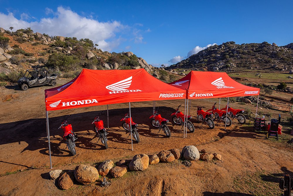 Eight CRF300Fs parked under several Honda canopies on a hillside.