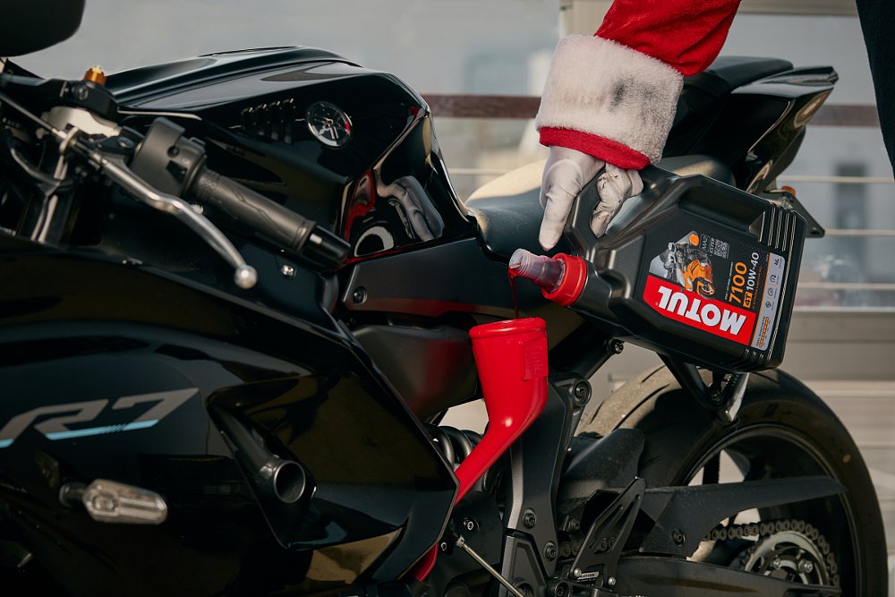 close view of a hand wearing a glove and a Santa Claus suit pouring Motul oil into a Yamaha YZF-R7