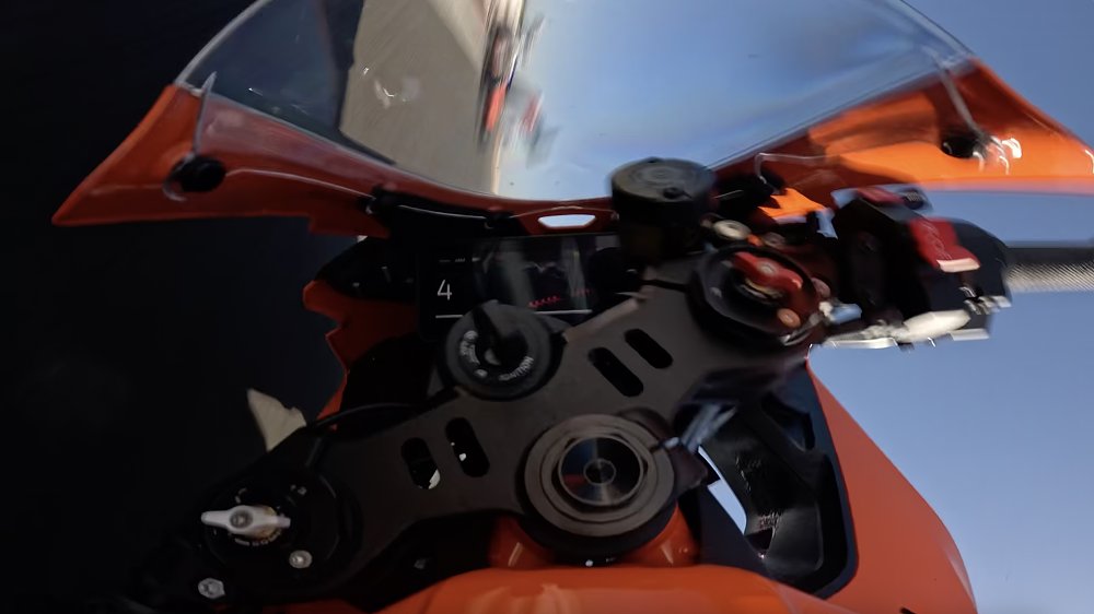 Onboard camera image from a motorcycle sliding down a racetrack in the middle of a crash, with the rider barely visible ahead on the track.