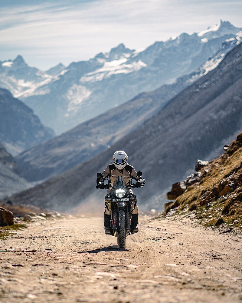 Dustin riding the Himalayan on a dirt road in the mountains in India, snow-covered peaks in the background