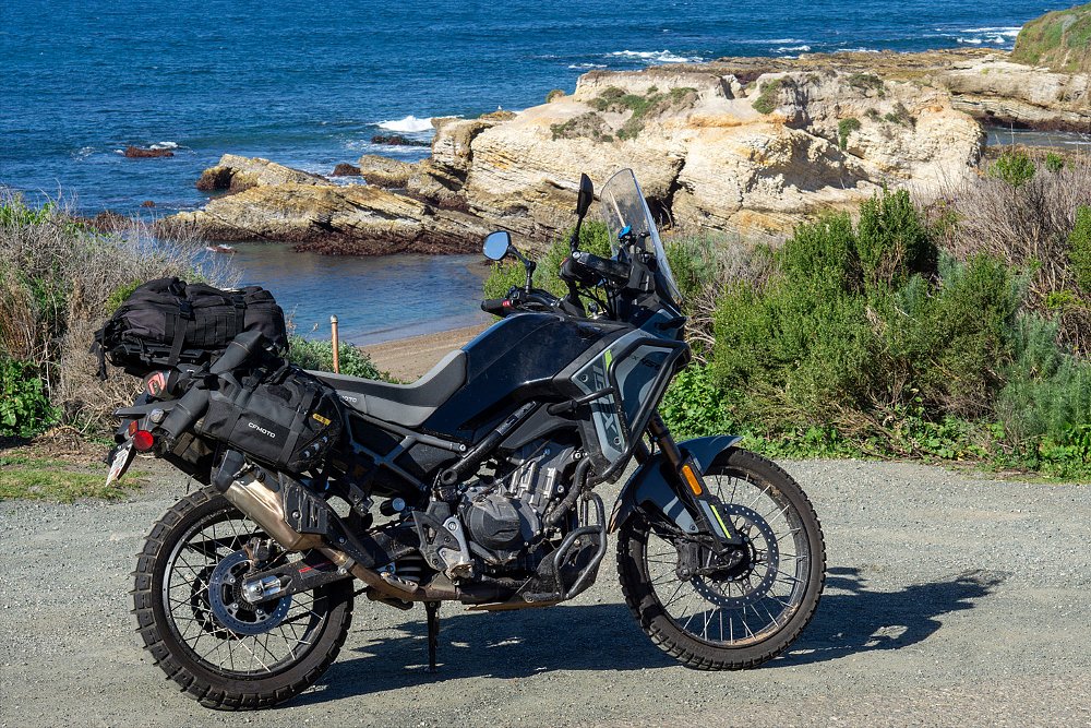 The CFMOTO Ibex 450 stands cliffside with a rocky beach in the distance.