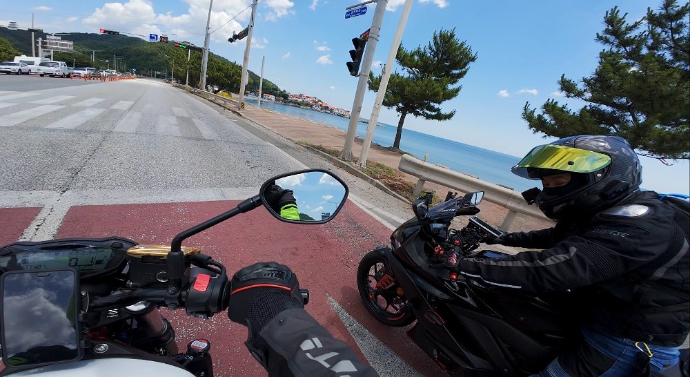 rider's view on the motorcycle, in a small seaside village, with another motorcyclist stopped alongside