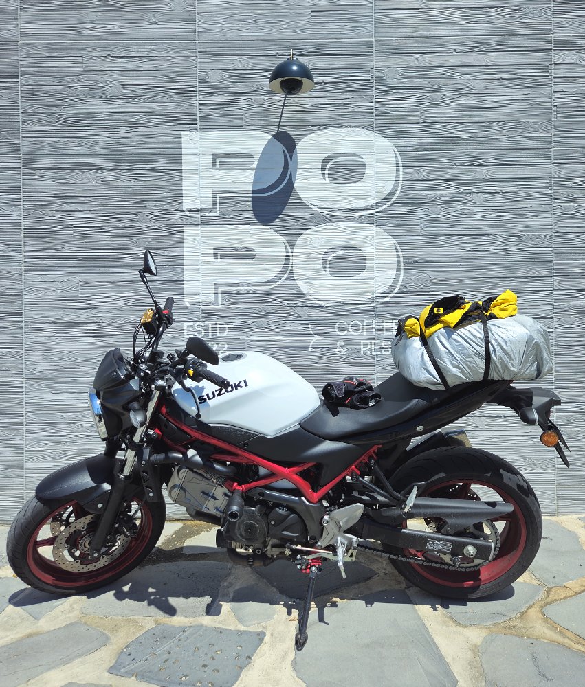 the white SV650 parked in front of a sign for a cafe with rain gear lying on the seat to dry in the sun