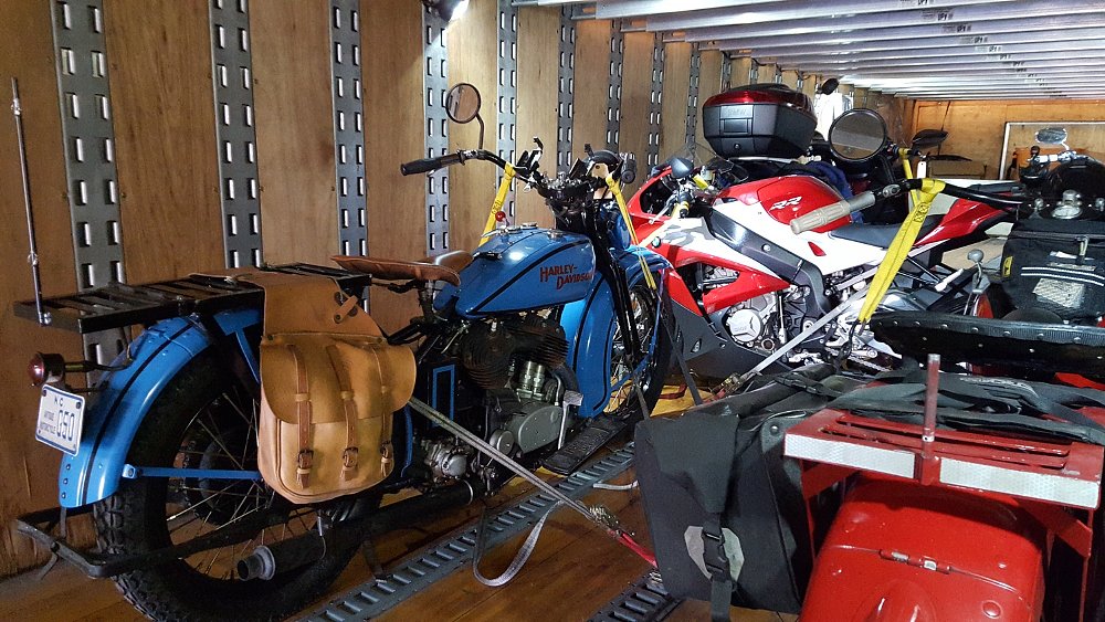 view of several motorcycles in the back of an enclosed truck, including a blue, antique Harley-Davidson