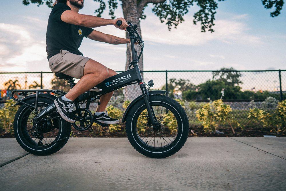 A man riding an e-bike along a bike path in shorts and a t-shirt.