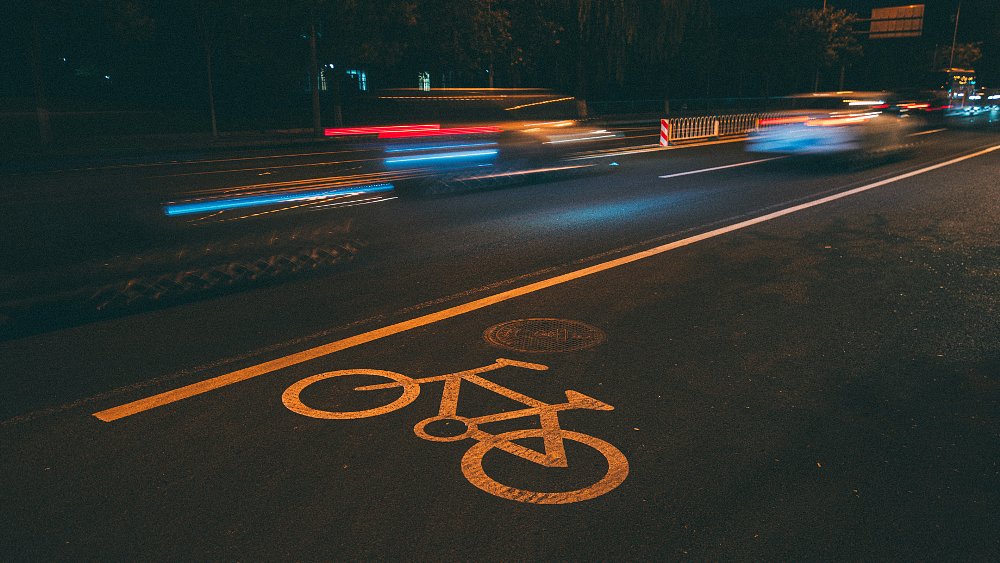 A bicycle lane, with logo in the foreground, at night with cars blurred as they drive by in the background.