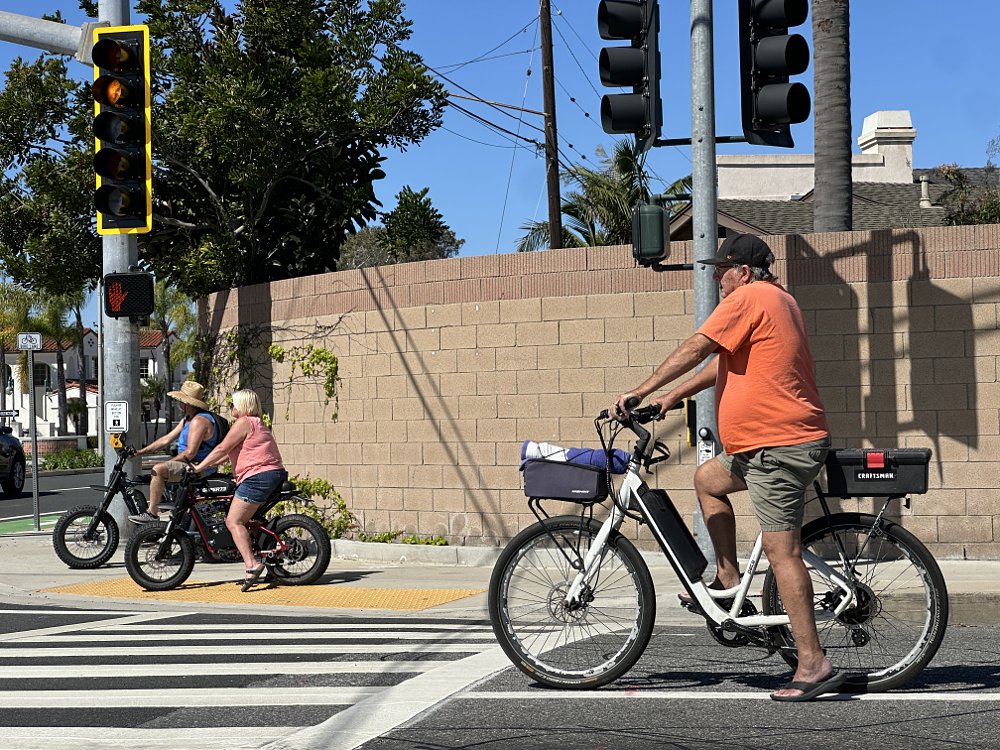 Three people wait at a traffic light on their e-bikes.