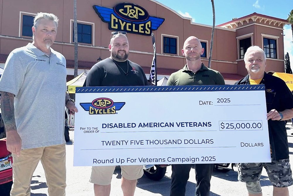 J&P Cycles and Disabled American Veterans representatives hold a $25,000 check with a J&P Cycles store in the background.