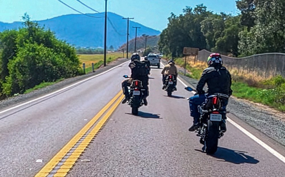 view of three riders ahead, behind a car, on a straight section of road, with the riders trying to find a comfortable position