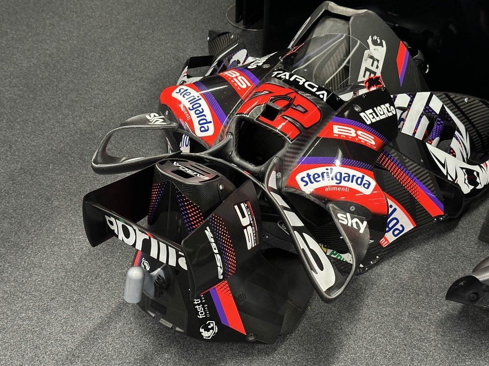 Pieces of carbon-fiber bodywork from Aprilia's RS-GP MotoGP motorcycle sit on the floor of a garage.