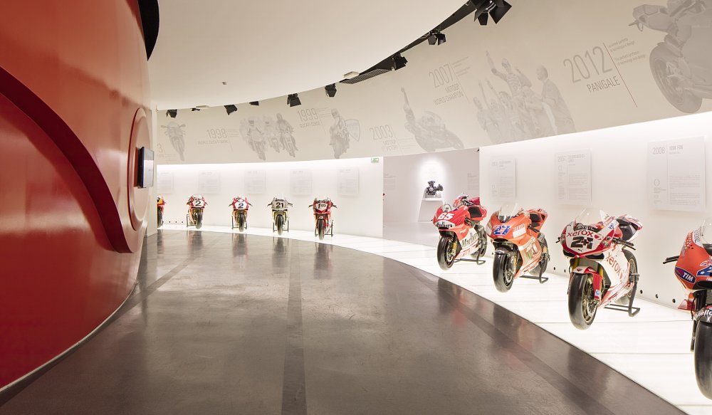 row of race bikes on display in a curved hallway in the Ducati Museum