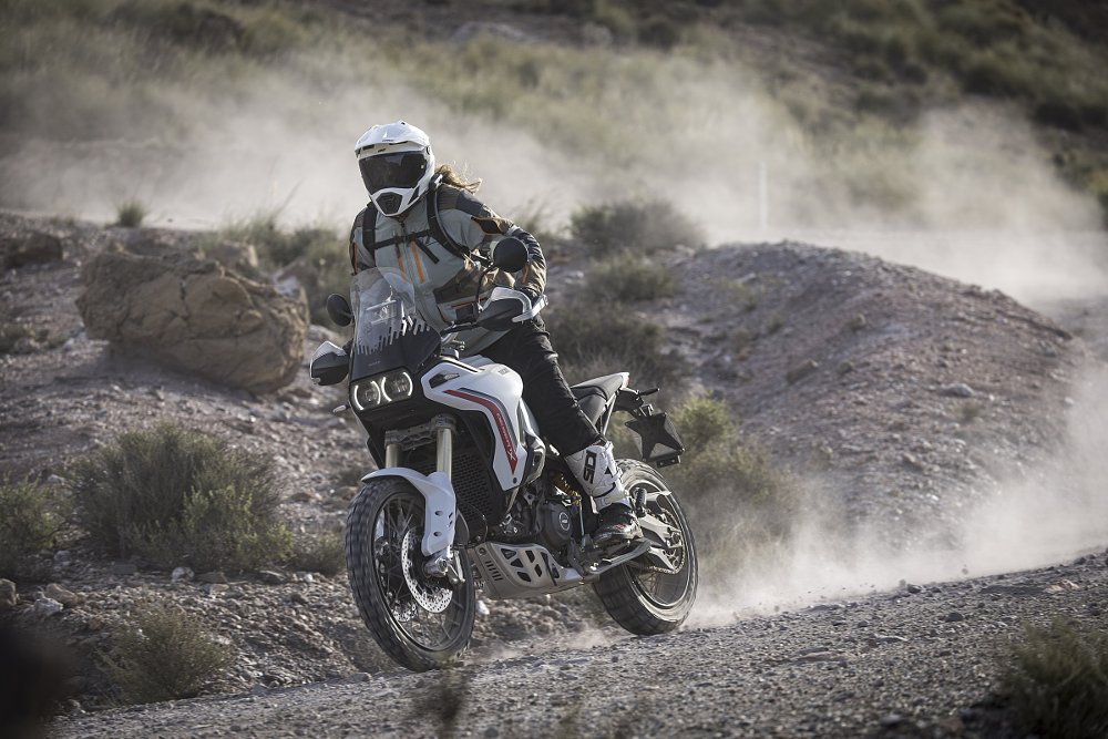 the rider on a gravel road on the DesertX, dust trailing behind