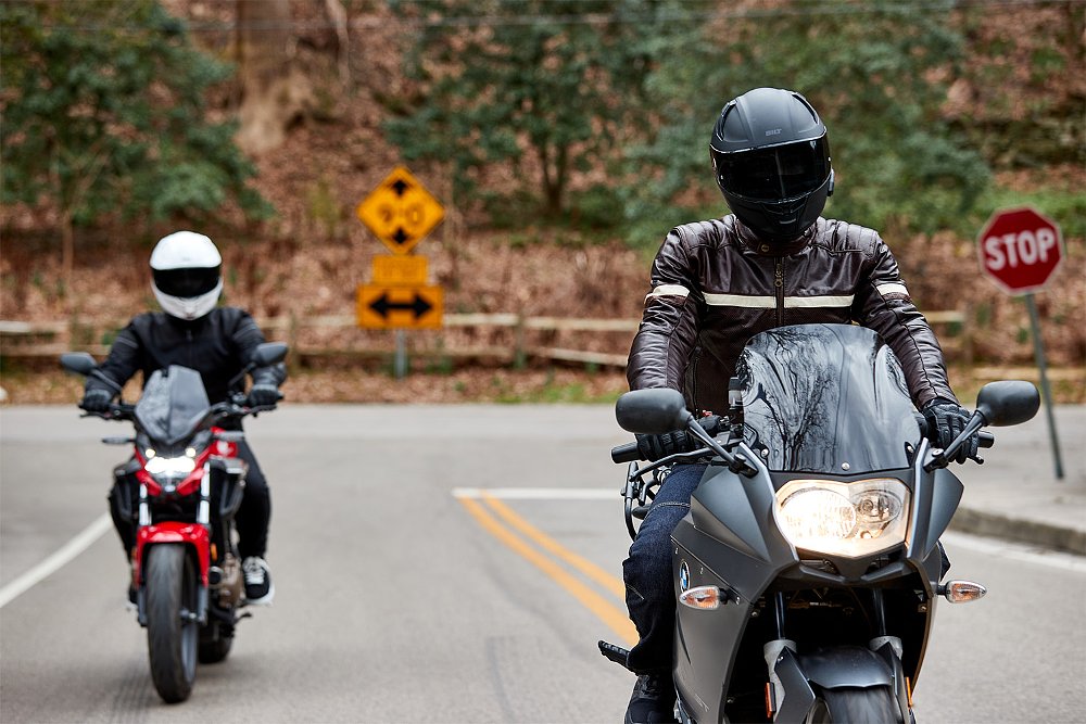 Two riders travel down a mountainside road.
