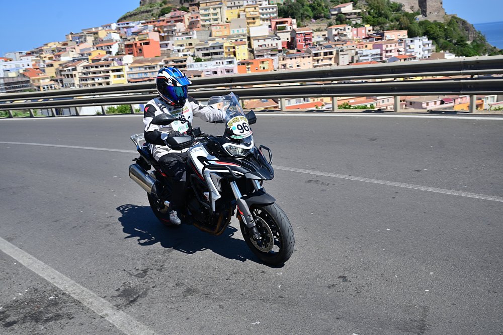 riding the TRK 702 on a two-lane road with an old hillside Sardinian village in the background