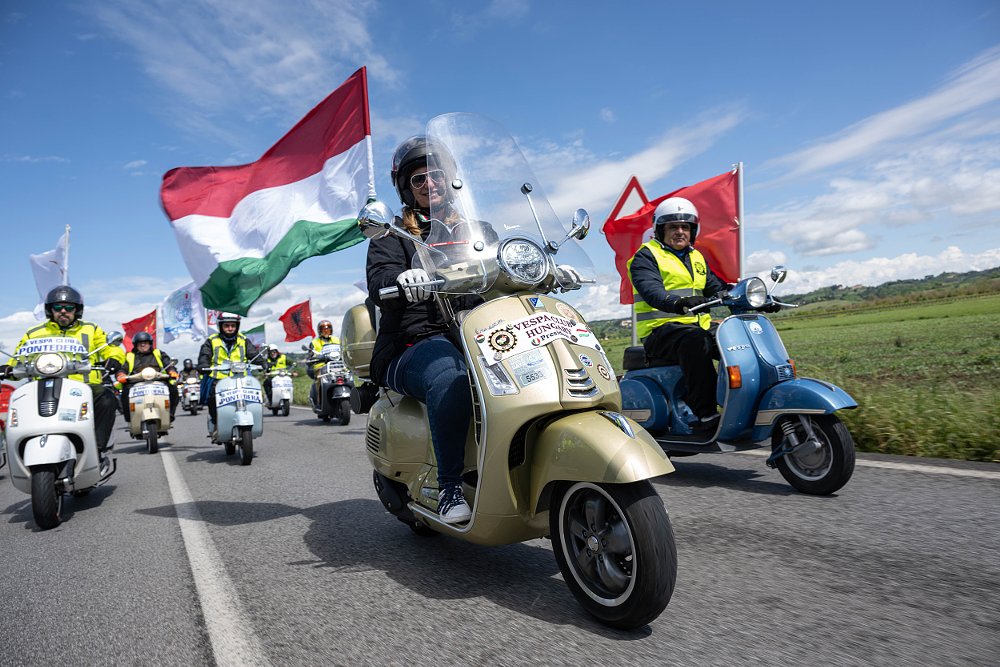 a group of Vespa riders from Hungary, flying the Italian flag on their scooters