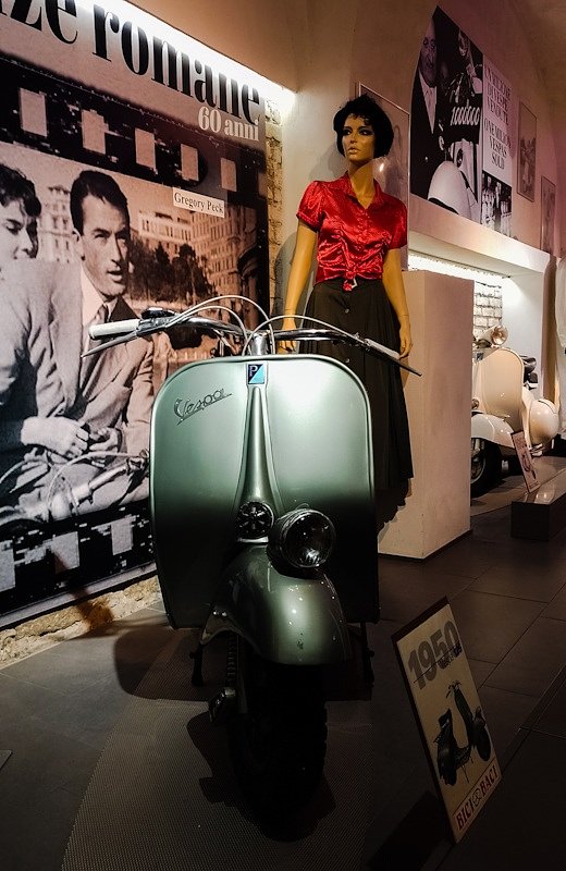 museum display of a scooter and a poster from the 'Roman Holiday' movie