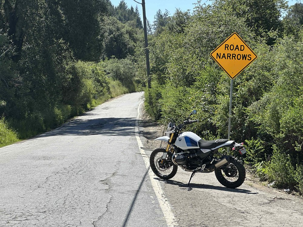 A 2026 BMW R 12 G/S parked along a single-lane, paved road near a sign reading 