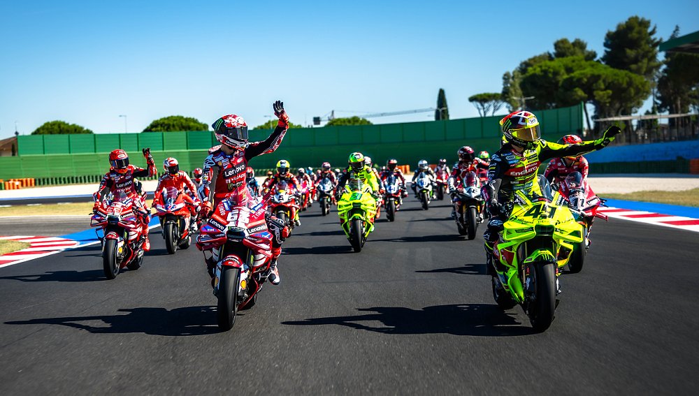 racers on a parade lap on the track, waving to fans