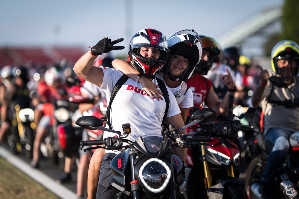 man and woman on a motorcycle smiling with a crowd of riders behind them