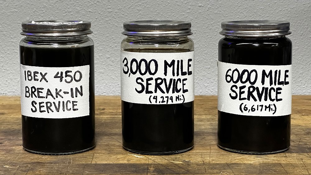 A close-up of three oil-filled jars on a work bench.