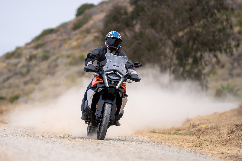 2027 KTM 1390 Super Adventure S EVO riding toward camera down a dusty gravel road.