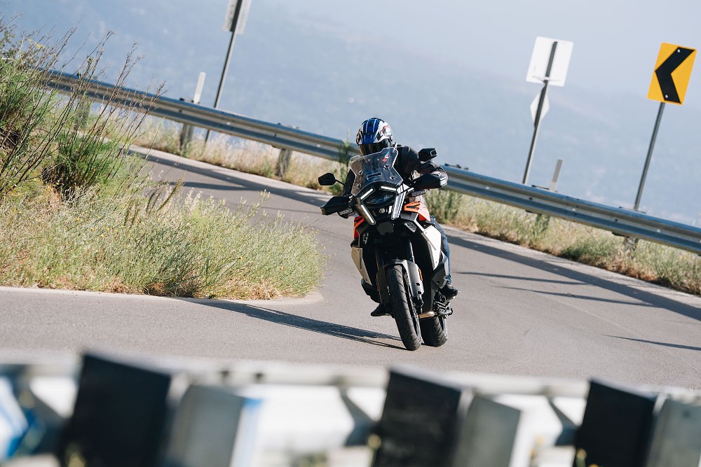 2027 KTM 1390 Super Adventure S EVO riding toward camera along a twisty, paved mountain road.