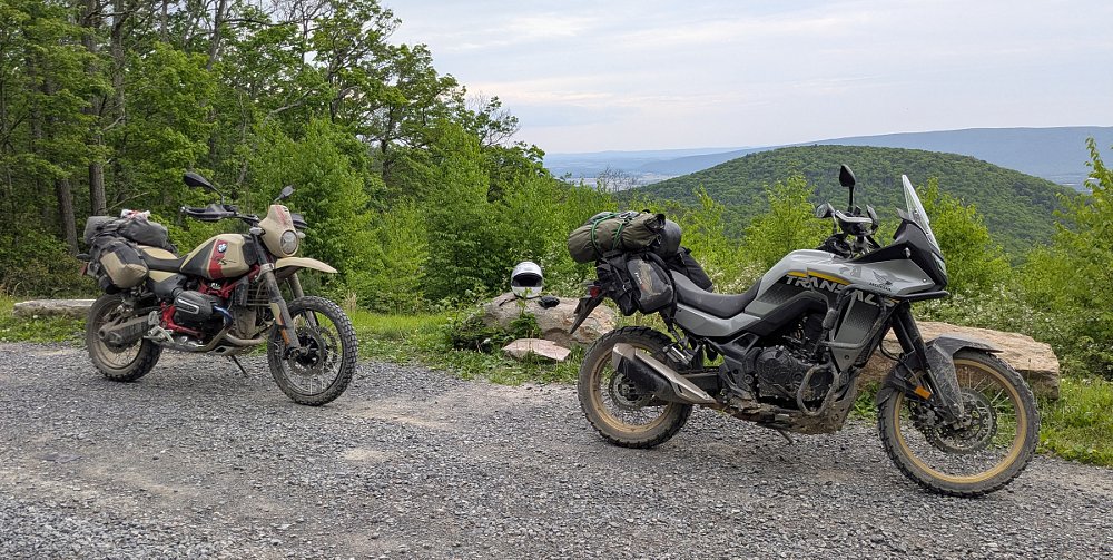 A gray Honda Transalp and the 'sand rover matte' colored BMW R 12 G/S at an overlook alongside a gravel road in the mountains