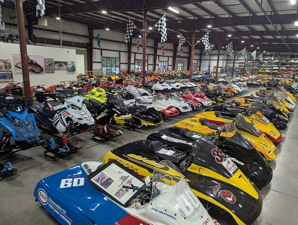 interior view of a warehouse stuffed with snowmobiles, some motorcycles, and a few cars