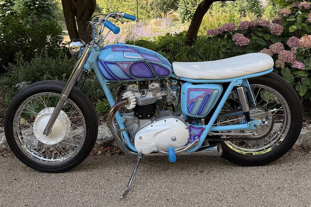 light blue Triumph motorcycle with intricate flames in the paint and a white seat