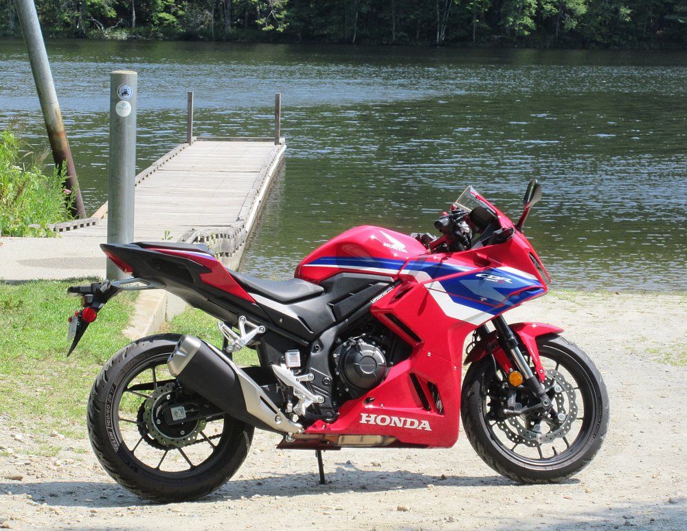 red CBR500R parked by a small pier sticking out into a lake in the woods