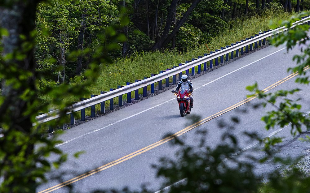 rider on the CBR500R on a country road viewed from a distance through trees