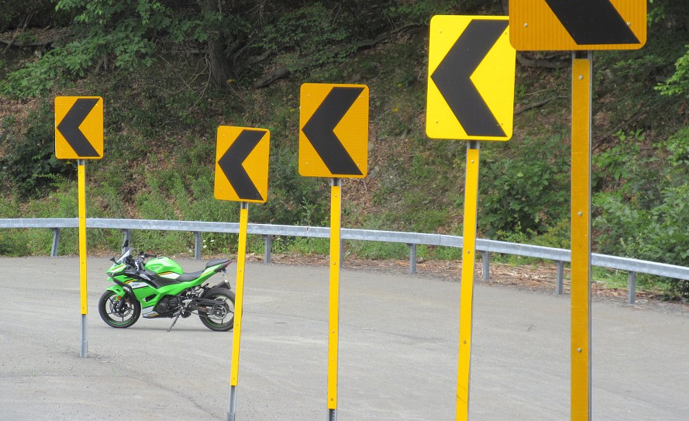 green Kawasaki Ninja 500 parked at the end of a row of yellow curve arrow signs