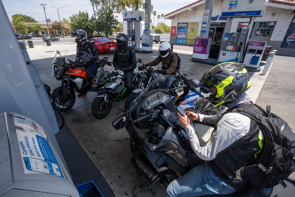 Five motorcycles parked at a gas station, filling up with fuel.