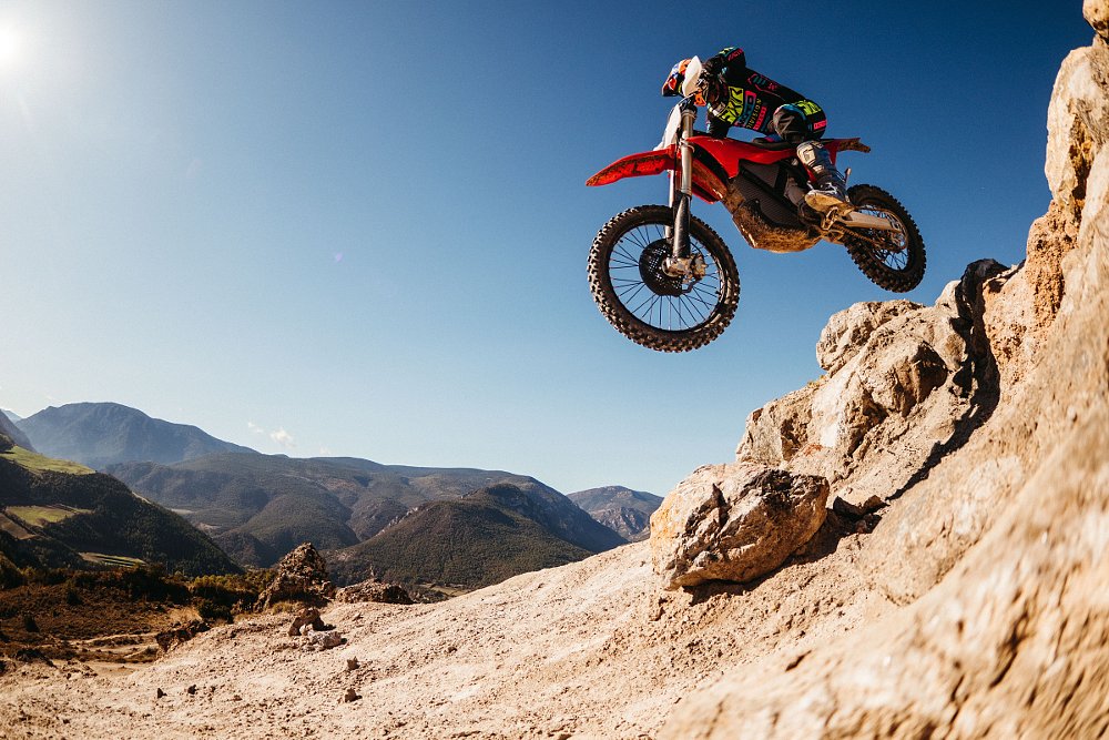 rider on a Stark VARG EX leaping off a jump on a mountainside