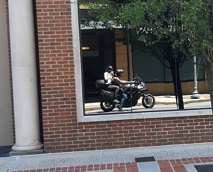 reflection in a storefront window of the two on their Multistrada motorcycle