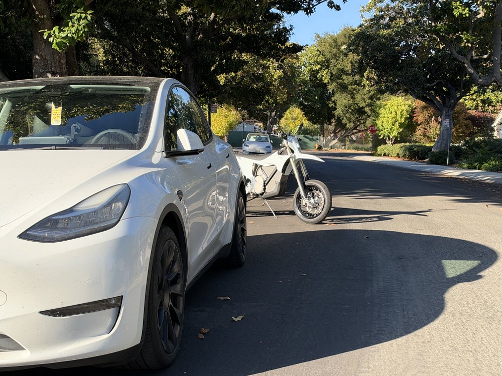2026 Stark VARG SM parked on a residential street with a Tesla Model Y in the foreground.