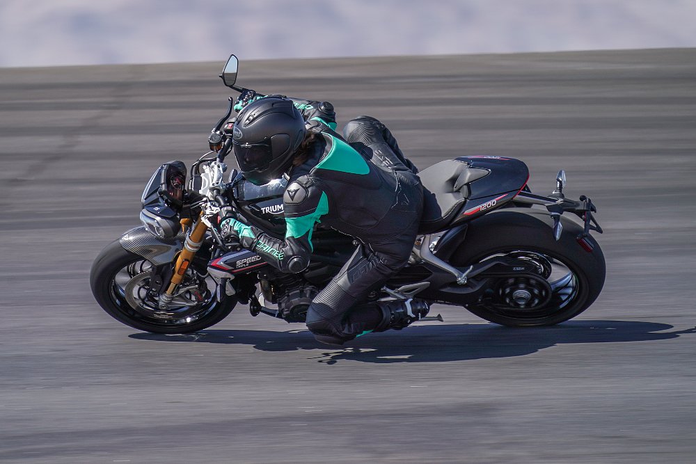 2022 Triumph Speed Triple 1200 RS being ridden by a female rider through a fast bowl corner at a racing circuit.