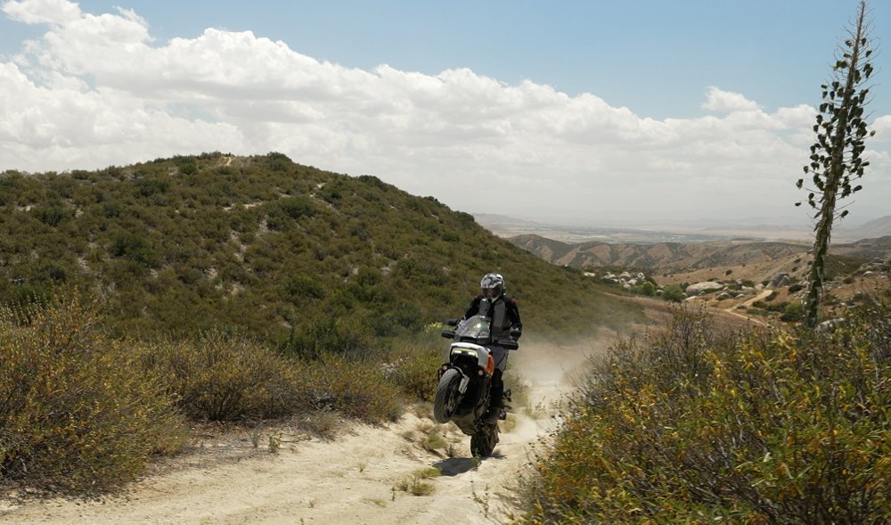 Harley-Davidson wheelying over a rut on a dirt road