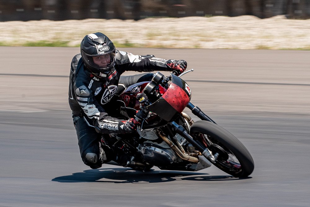 Alyssa rides her motorcycle fast on the track straight at the camera.