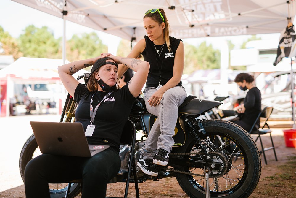 Bree Poland and Melissa Paris sitting together near a motorcycle in deep conversation.