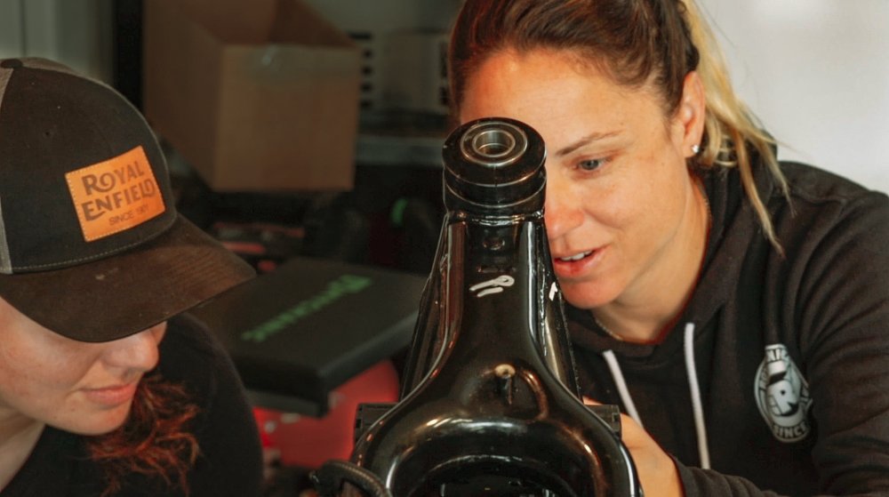 Melissa and Alyssa peer in close at the motorcycle frame to measure up their next cut.