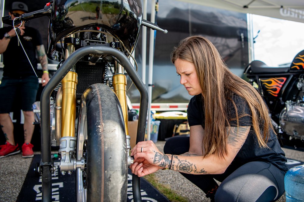 Michaela uses a wrench to work on the front tire of her motorcycle.