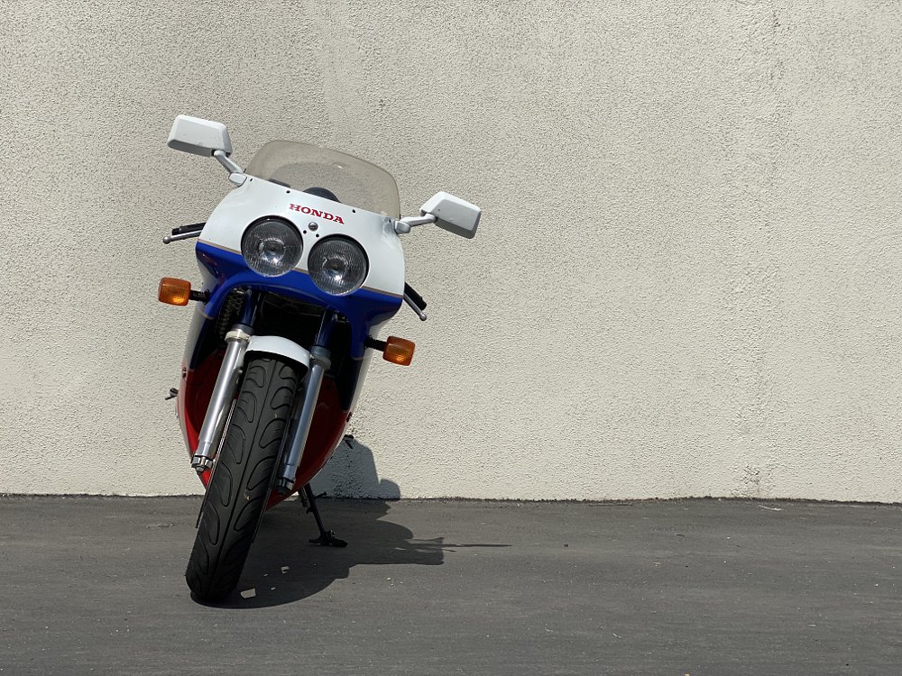The front of a Honda RC30 on a kick stand in front of a gray wall.