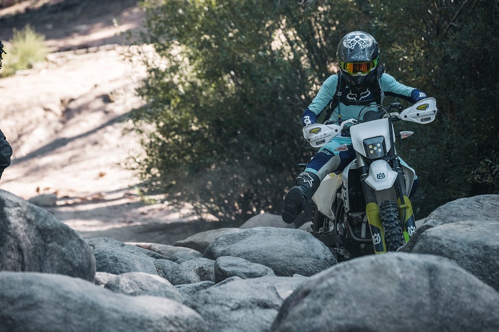 A female rider lifts their foot to overcome very large rocks on board her husqvarna dual sport motorcycle