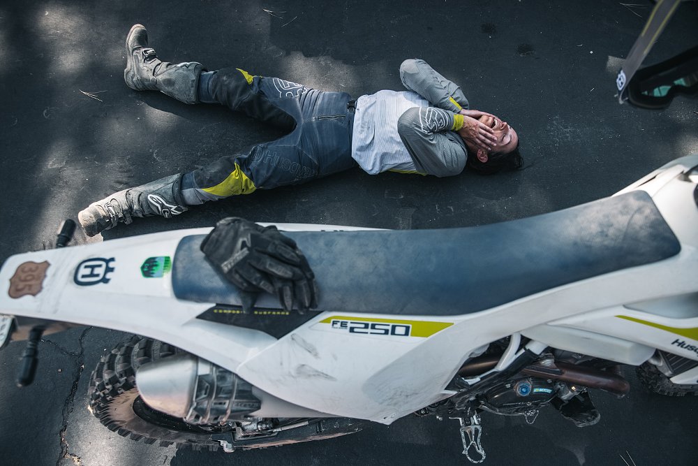 A female rider rests on the pavement next to her motorcycle.