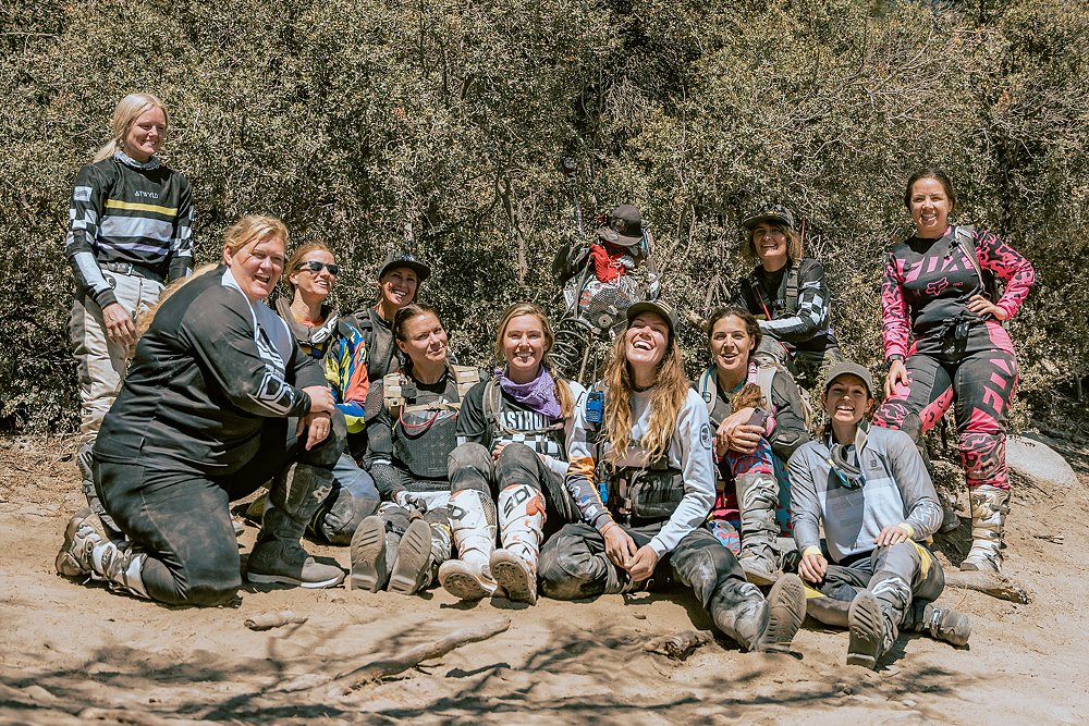 The female riders gather in a group for a photo with a sculpture made from junk parts on the john Bull trail