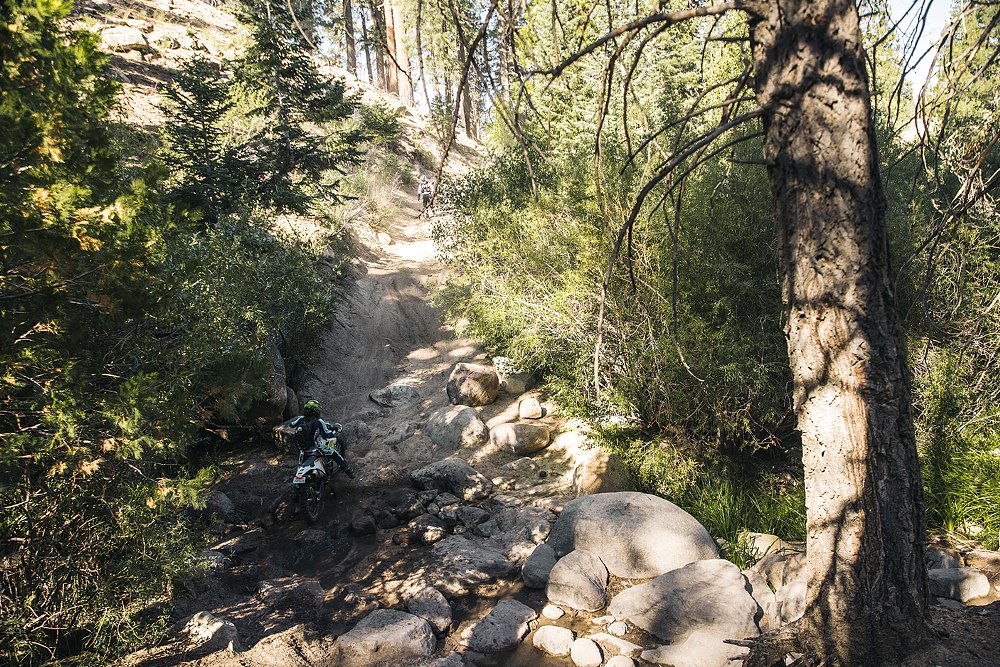 A female rider attempts to climb a steep rocky hill on her motorcycle