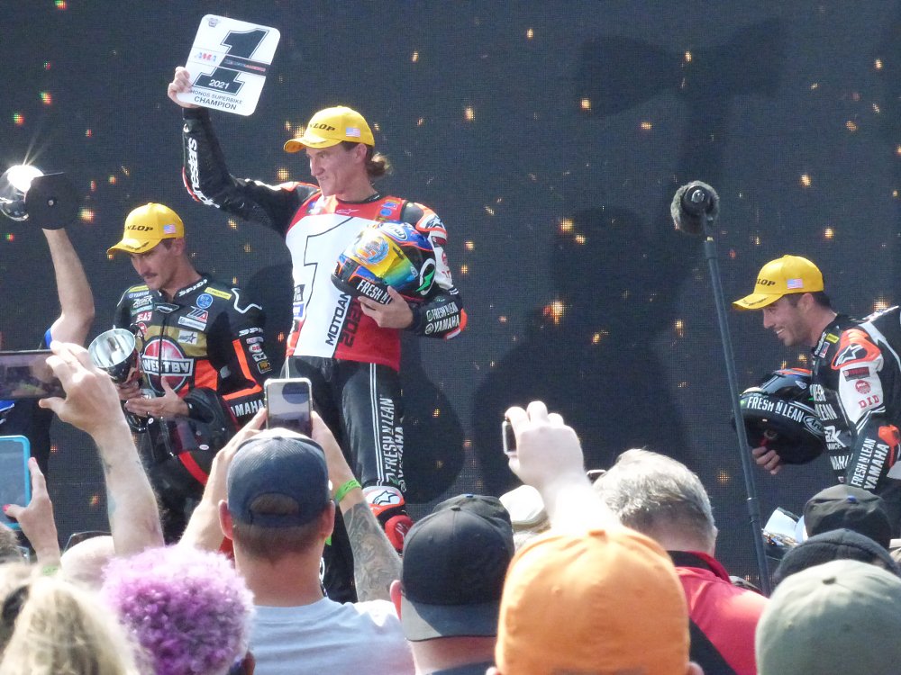 Gagne holds up number one plate on the podium