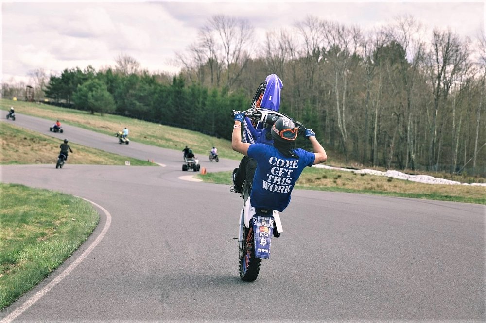 young dirt bike rider does a wheelie on a race track
